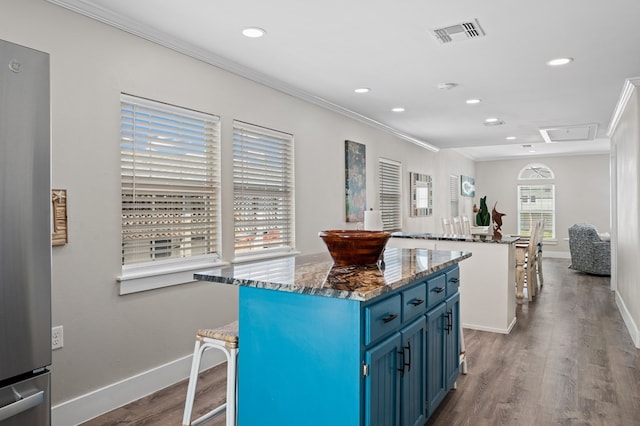 kitchen with a breakfast bar, dark wood-type flooring, blue cabinets, a kitchen island, and stainless steel refrigerator