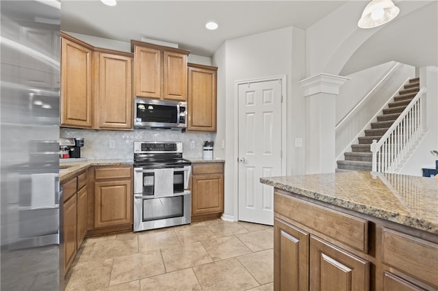 kitchen featuring stainless steel appliances, light stone countertops, light tile patterned floors, backsplash, and decorative columns