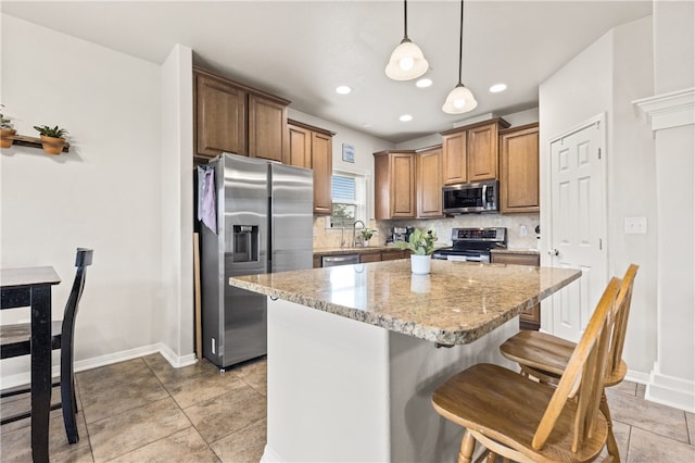 kitchen with stainless steel appliances, a kitchen island, light stone countertops, hanging light fixtures, and a breakfast bar area