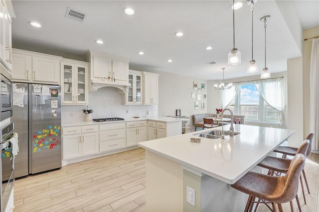 kitchen with a breakfast bar, a kitchen island with sink, hanging light fixtures, sink, and appliances with stainless steel finishes