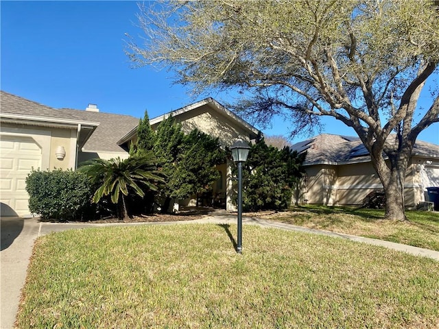 view of front of home with a garage, stucco siding, a shingled roof, and a front yard