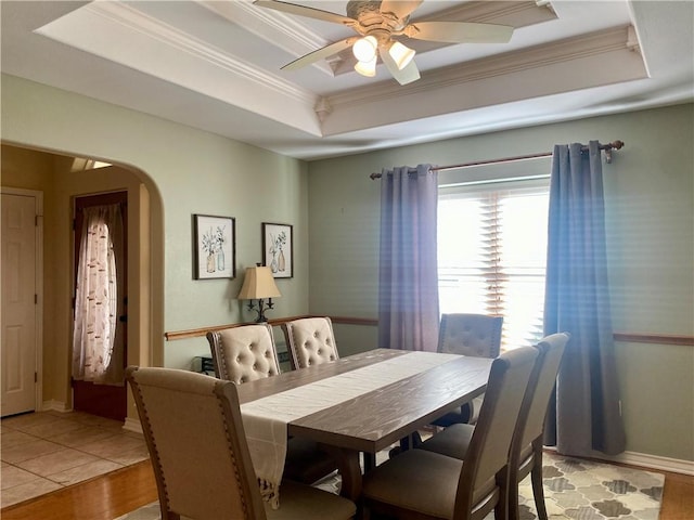 dining space featuring ceiling fan, a raised ceiling, arched walkways, and ornamental molding