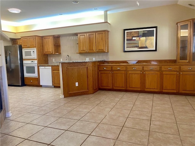 kitchen featuring light tile patterned floors, white appliances, tasteful backsplash, and brown cabinetry