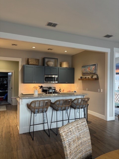 kitchen featuring stove, stainless steel microwave, a breakfast bar area, and visible vents