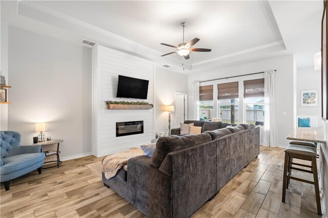 living area featuring a fireplace, visible vents, baseboards, wood tiled floor, and a raised ceiling