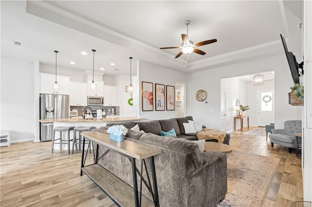 living room featuring ornamental molding, light wood-type flooring, a raised ceiling, and a ceiling fan