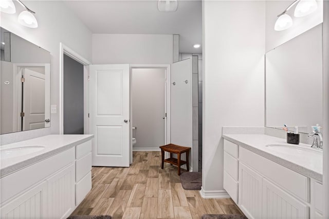 full bath with a sink, toilet, two vanities, and wood finished floors