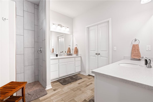 full bathroom with two vanities, a sink, tiled shower, and wood finished floors