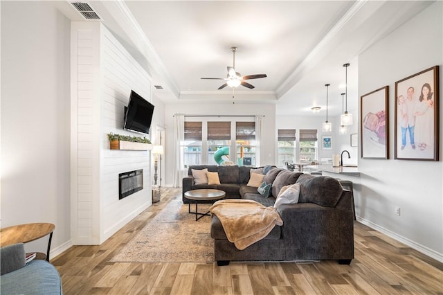 living room with light wood-style floors, a raised ceiling, visible vents, and crown molding