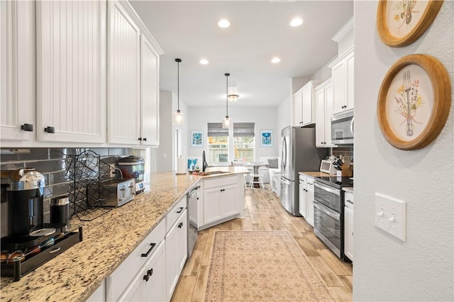 kitchen with a peninsula, wood finish floors, a sink, white cabinets, and appliances with stainless steel finishes