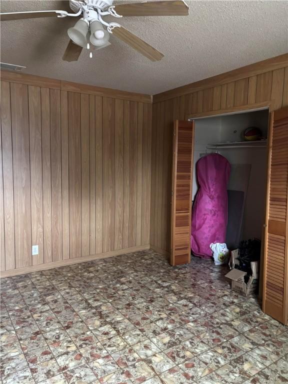 unfurnished bedroom with ceiling fan, a closet, and wood walls