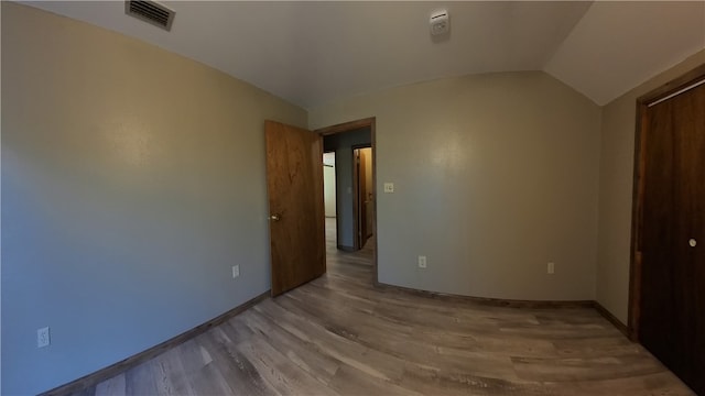 unfurnished bedroom featuring light hardwood / wood-style floors, lofted ceiling, and a closet