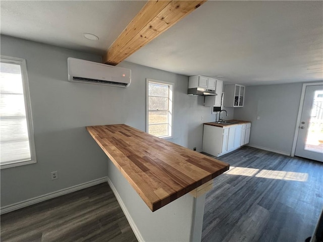 kitchen featuring a peninsula, a sink, white cabinetry, baseboards, and an AC wall unit