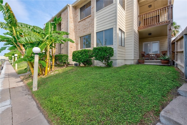 view of side of home featuring a lawn, a balcony, and french doors