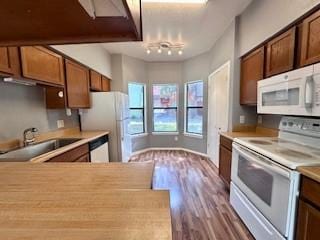 kitchen with a sink, white appliances, light countertops, baseboards, and dark wood-style floors