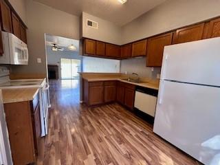 kitchen featuring light countertops, brown cabinetry, white appliances, and wood finished floors