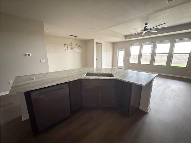 kitchen featuring light stone counters, open floor plan, a tray ceiling, dark wood finished floors, and decorative light fixtures