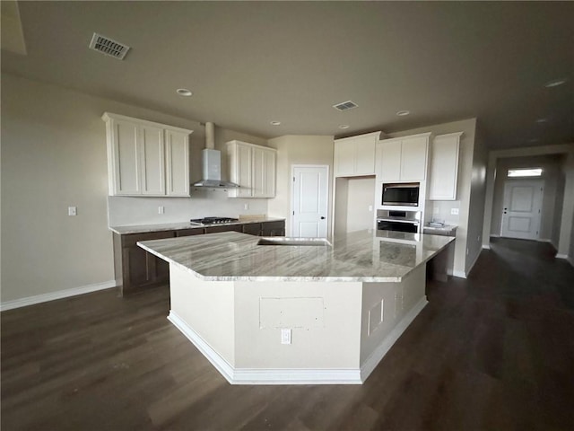 kitchen with appliances with stainless steel finishes, wall chimney exhaust hood, white cabinetry, and a spacious island