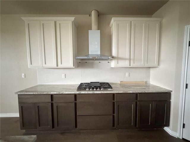 kitchen featuring wall chimney exhaust hood, stainless steel gas stovetop, white cabinetry, and light stone counters