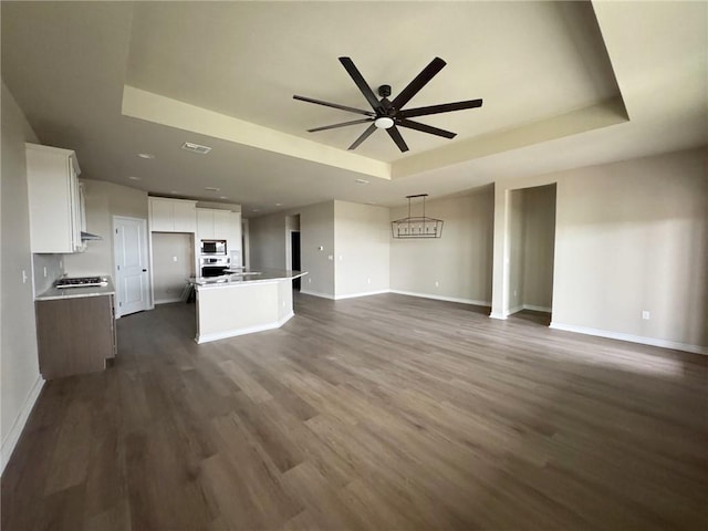 unfurnished living room with ceiling fan, a tray ceiling, and baseboards