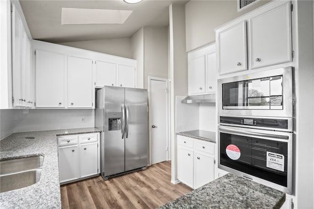 kitchen with light stone counters, stainless steel appliances, lofted ceiling with skylight, wood-type flooring, and white cabinets