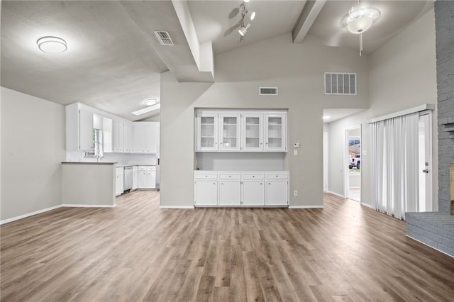 unfurnished living room featuring lofted ceiling with beams, plenty of natural light, light wood-type flooring, and a brick fireplace