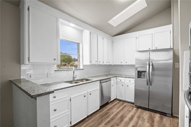 kitchen featuring vaulted ceiling with skylight, white cabinets, sink, and appliances with stainless steel finishes