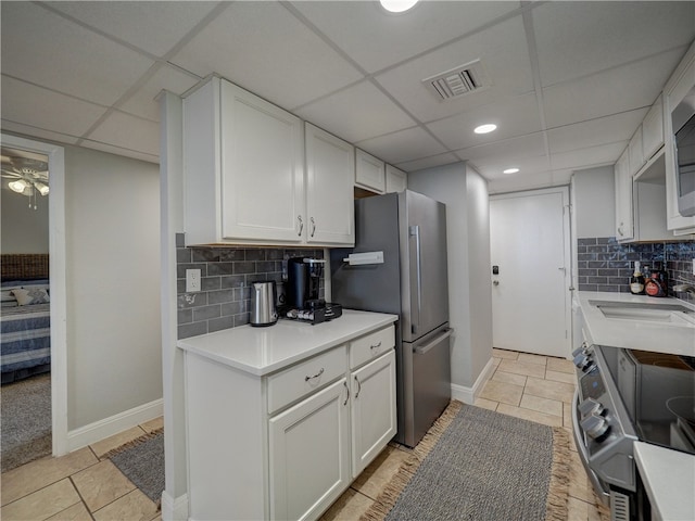 kitchen featuring white cabinets, appliances with stainless steel finishes, a paneled ceiling, and tasteful backsplash