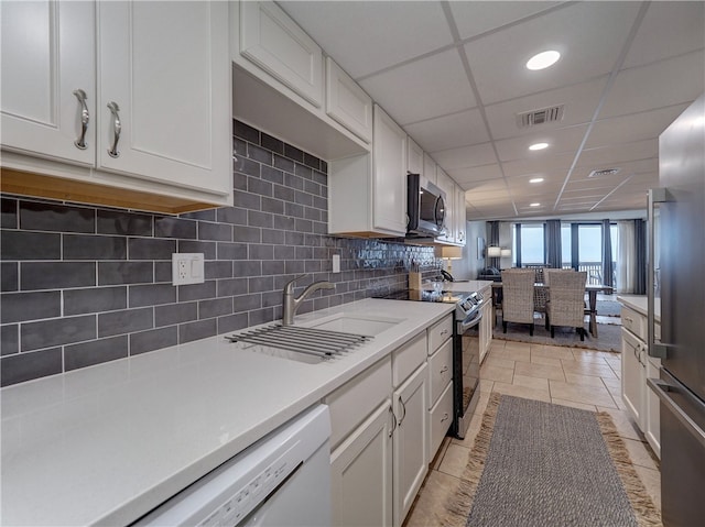 kitchen featuring a drop ceiling, white cabinets, light tile patterned floors, sink, and appliances with stainless steel finishes