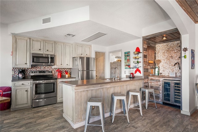 kitchen featuring appliances with stainless steel finishes, dark hardwood / wood-style flooring, a kitchen breakfast bar, beverage cooler, and kitchen peninsula