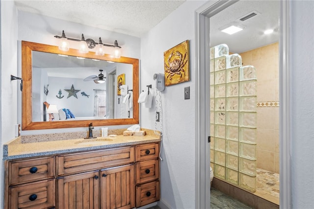 bathroom with ceiling fan, a textured ceiling, a tile shower, hardwood / wood-style floors, and vanity