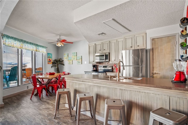 kitchen featuring cream cabinets, hardwood / wood-style floors, ceiling fan, a breakfast bar, and appliances with stainless steel finishes