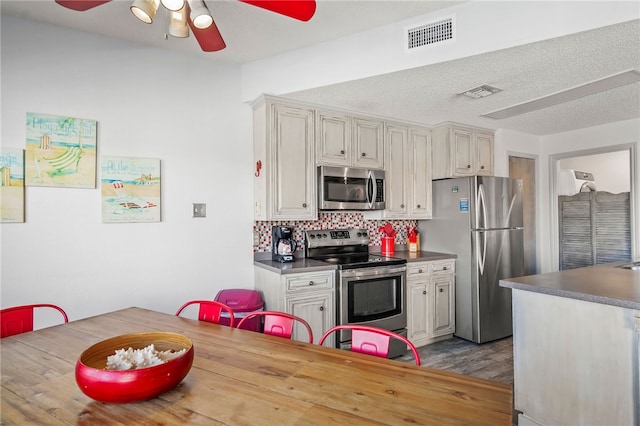 kitchen featuring stainless steel appliances, ceiling fan, a textured ceiling, light wood-type flooring, and decorative backsplash