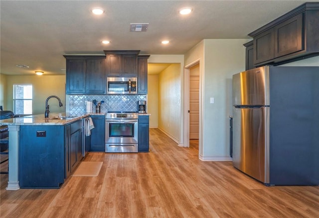 kitchen with sink, light stone counters, kitchen peninsula, stainless steel appliances, and light hardwood / wood-style flooring