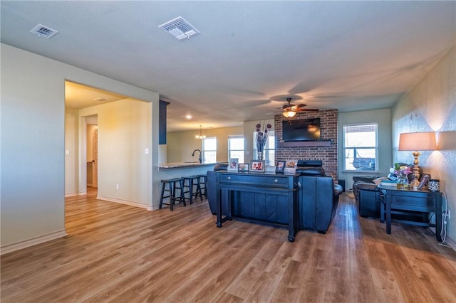 living room featuring sink, hardwood / wood-style flooring, ceiling fan with notable chandelier, and a brick fireplace