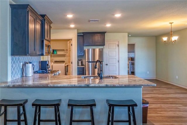 kitchen with sink, light wood-type flooring, stainless steel appliances, washer / clothes dryer, and decorative backsplash