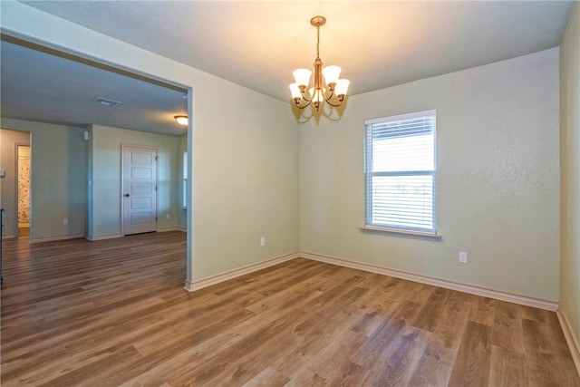 empty room with a notable chandelier and hardwood / wood-style flooring