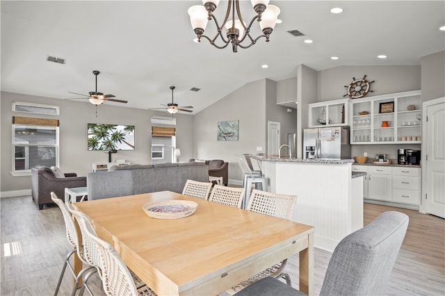 dining space featuring ceiling fan with notable chandelier, light hardwood / wood-style floors, vaulted ceiling, and sink