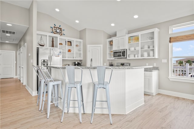 kitchen with white cabinets, appliances with stainless steel finishes, light stone countertops, and light hardwood / wood-style floors