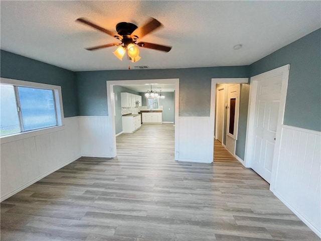 4313 Molina Dr, Corpus Christi, TX 78416 - spare room featuring a wainscoted wall, a ceiling fan, a chandelier, light wood-style floors, and a textured ceiling
