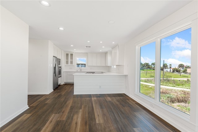 kitchen featuring dark hardwood / wood-style flooring, kitchen peninsula, sink, stainless steel fridge with ice dispenser, and white cabinetry