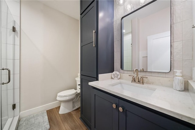 full bath featuring a shower stall, wood finished floors, toilet, vanity, and baseboards