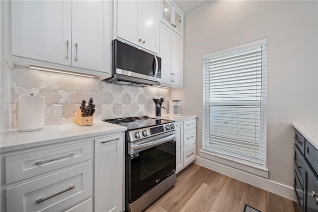 kitchen with light wood finished floors, tasteful backsplash, appliances with stainless steel finishes, and white cabinetry