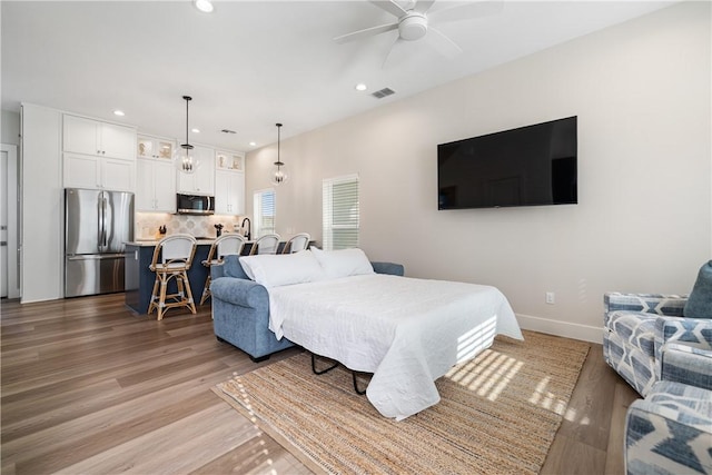 bedroom featuring light wood finished floors, baseboards, stainless steel refrigerator, visible vents, and recessed lighting