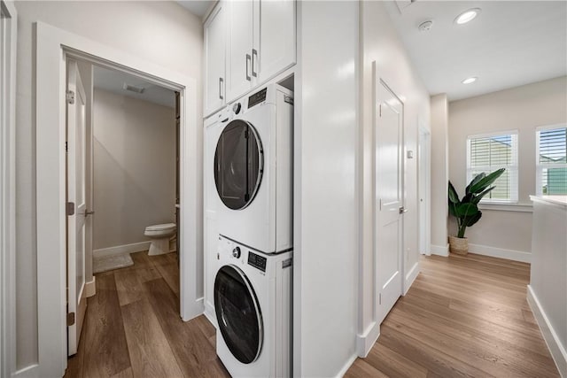 clothes washing area with light wood-type flooring, baseboards, stacked washing maching and dryer, and recessed lighting