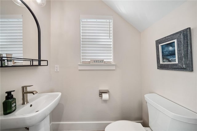 half bath featuring lofted ceiling, toilet, and a sink