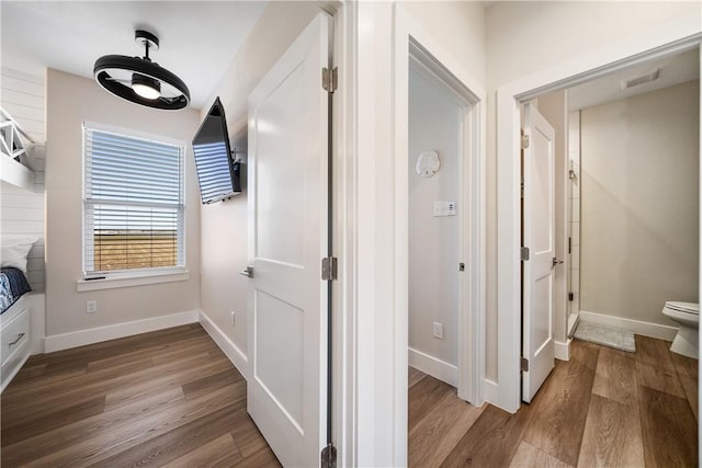 corridor featuring wood finished floors, visible vents, and baseboards