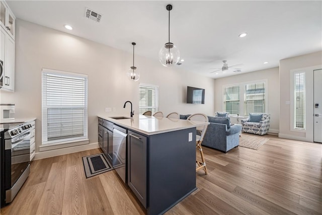 kitchen featuring a kitchen breakfast bar, a sink, light wood-style floors, a peninsula, and appliances with stainless steel finishes