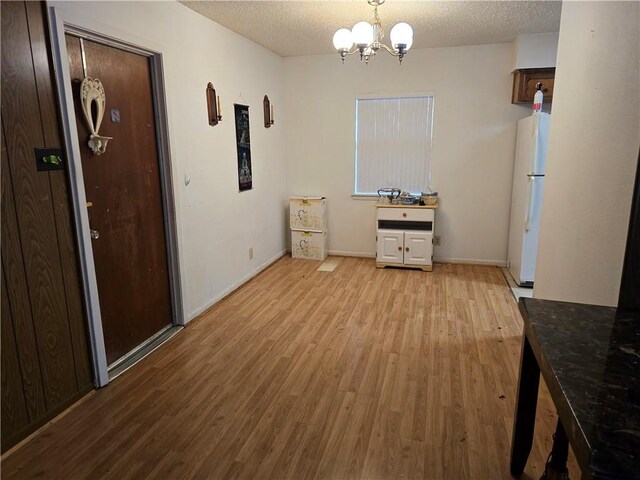 unfurnished dining area featuring an inviting chandelier, baseboards, light wood finished floors, and a textured ceiling