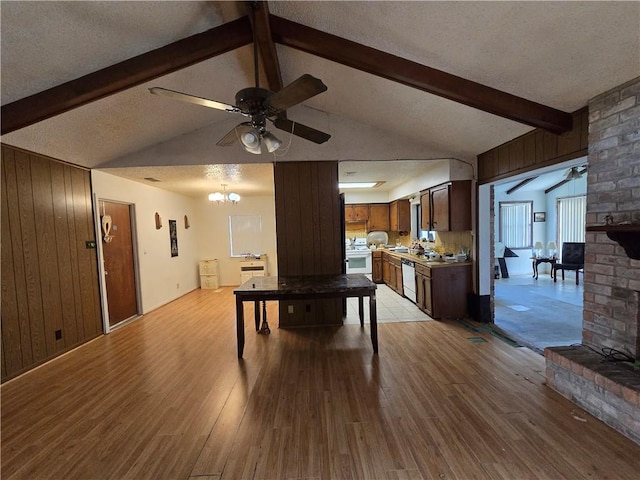 game room featuring ceiling fan with notable chandelier, a textured ceiling, wood walls, and light wood finished floors